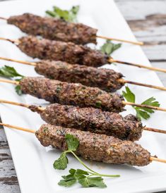 several skewers of meat with parsley on them sitting on a white plate