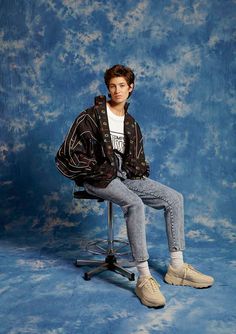 a young man sitting on top of a chair in front of a blue backdrop with clouds