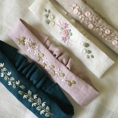 four different colored headbands are laying on a white tablecloth with embroidered flowers and leaves