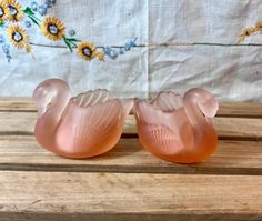 two pink glass swans sitting on top of a wooden table