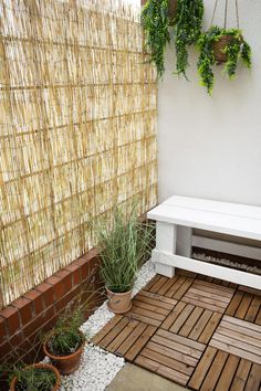 a white bench sitting on top of a wooden floor next to potted plants and a bamboo fence