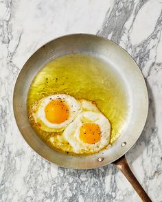 two fried eggs in a frying pan on a marble counter