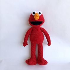 a crocheted red stuffed animal with big eyes and an orange nose, standing on a white background