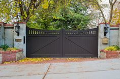 a gated entrance to a home with trees in the back ground and leaves on the ground