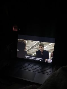 a laptop computer sitting on top of a bed in the dark with someone watching it