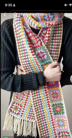 a woman wearing a multicolored crocheted scarf with fringes on it