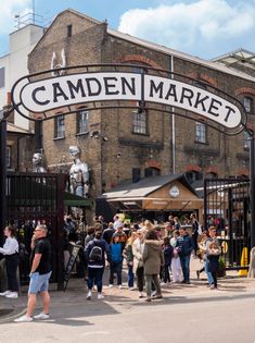 a crowd of people standing under an open market sign in front of a brick building