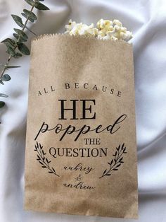 a brown paper bag with the words he popped the question next to some white flowers