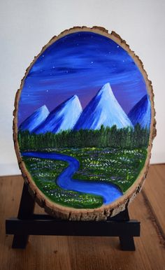 a painting on a piece of wood that is sitting on a wooden stand with a river and mountains in the background