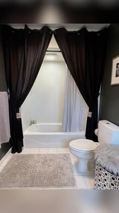 a white toilet sitting next to a bath tub in a bathroom with black curtains on the windows