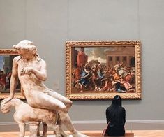 a woman sitting on a bench in front of a painting and another person looking at it