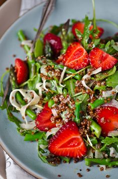 a salad with strawberries and greens on a blue plate