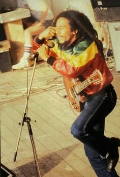 a man with dreadlocks is singing into a microphone and playing an electric guitar