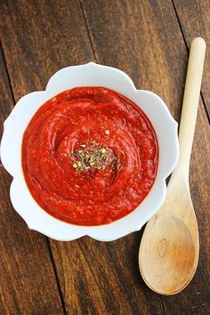 a white bowl filled with red sauce next to a wooden spoon on top of a table