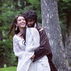 a man and woman dressed in medieval clothing hugging each other while walking through the woods