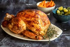 a roasted turkey sits on a plate with carrots and brussel sprouts