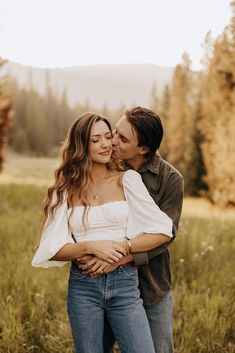 a man and woman are standing in the grass with their arms around each other as they kiss