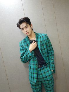 a young man in a green and black plaid suit standing next to a white wall