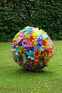 a colorful ball made out of plastic flowers on the grass in front of some bushes