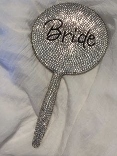 there is a silver sparkle fan with the word bride on it's side, sitting on a white sheet