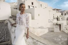 a woman in a white wedding dress standing on a stone wall next to some buildings