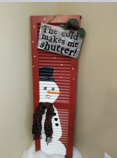 a red shutter with a snowman painted on it and a sign that says the cold makes me shuter