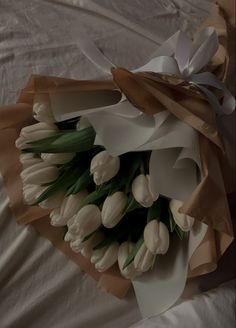 a bouquet of white tulips wrapped in brown paper on a bed with sheets