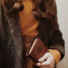 a woman holding a book in her right hand and wearing a brown dress underneath it