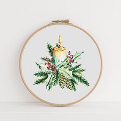 a cross stitch christmas ornament with a lit candle and holly wreath on it