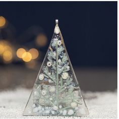 a glass christmas tree with white and blue decorations on it's sides sitting in the snow