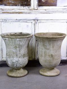 two cement planters sitting next to each other in front of a white door with peeling paint