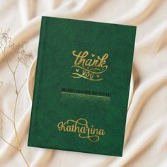 a green book with the words thank you written in gold on it next to some dried flowers