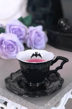 a black and white cup with pink liquid in it on a saucer next to purple roses