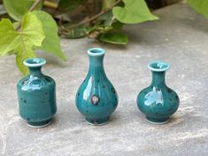 three blue vases sitting next to each other on a stone surface with leaves in the background