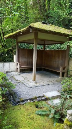 a small wooden shelter in the middle of a lush green area with rocks and plants