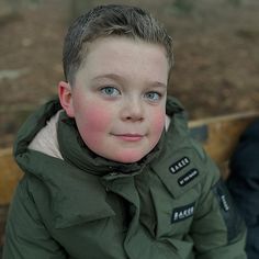 a young boy wearing a green jacket and blue eyes