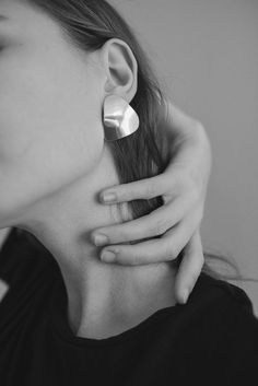 a woman with her hand on the back of her neck, wearing two silver heart shaped earrings