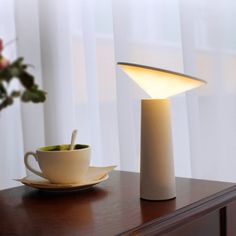 a white table lamp sitting on top of a wooden table next to a cup and saucer