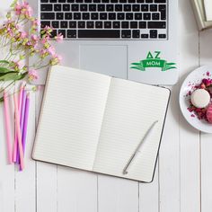 an open notebook sitting on top of a desk next to a laptop computer and flowers