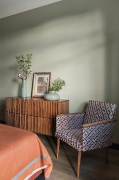 a bed room with a neatly made bed next to a chair and a dresser in front of it