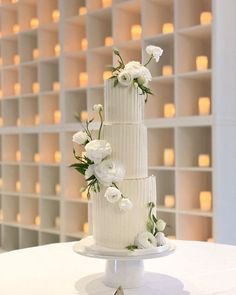 a three tiered white wedding cake with flowers on the side and candles behind it