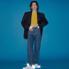 a woman standing in front of a blue background with her hands on her hips, wearing jeans and a blazer