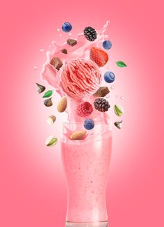 an ice cream sundae with berries, nuts and milk splashing into it on a pink background