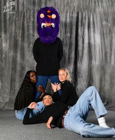 a group of people posing in front of a photo booth with a purple monster mask on their head