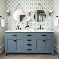 two sinks and mirrors in a bathroom with wallpaper on the back drop off walls