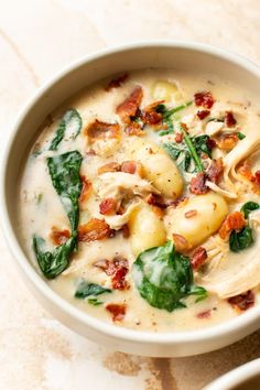 a white bowl filled with pasta and spinach on top of a marble countertop