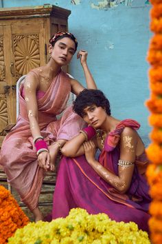 two women sitting next to each other in front of flowers and an old wooden cabinet