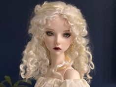 a close up of a doll with blonde hair and green eyes wearing a white dress