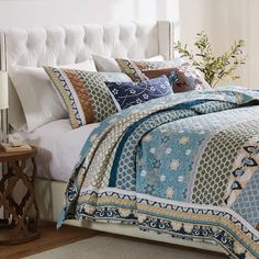 a bed covered in blue and white quilts with pillows next to a night stand