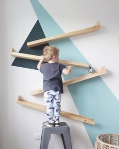 a little boy standing on top of a step stool in front of a painted wall